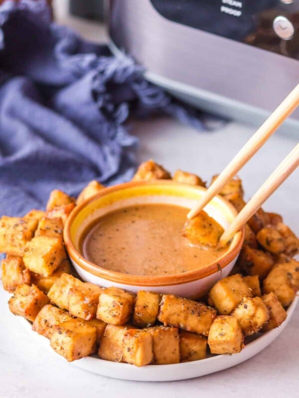 POV chopsticks dipping into a plate of air fryer tofu with a dish of sauce in the center