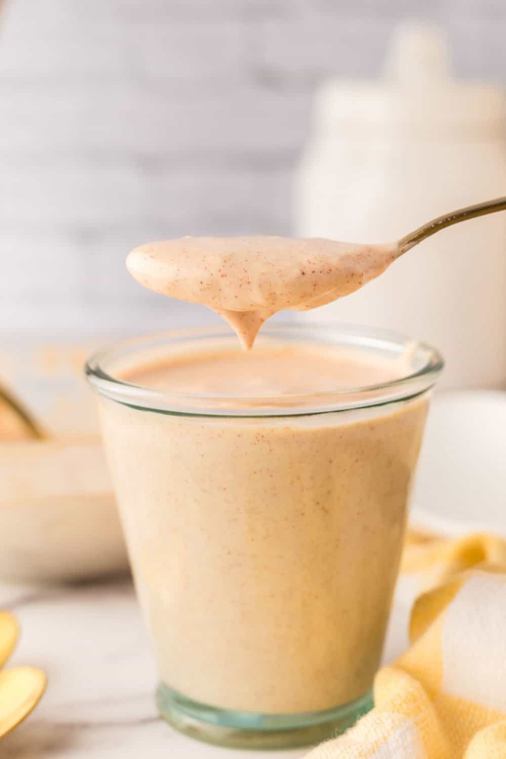 small glass jar of Alabama white sauce being spooned out with a golden spoon.