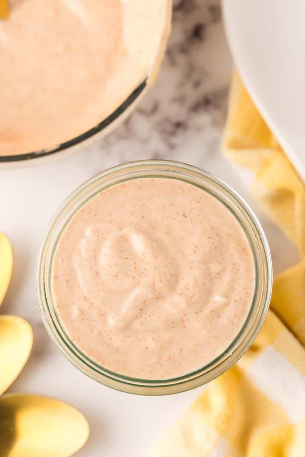 small glass jar of Alabama white sauce with golden spoons to the side.