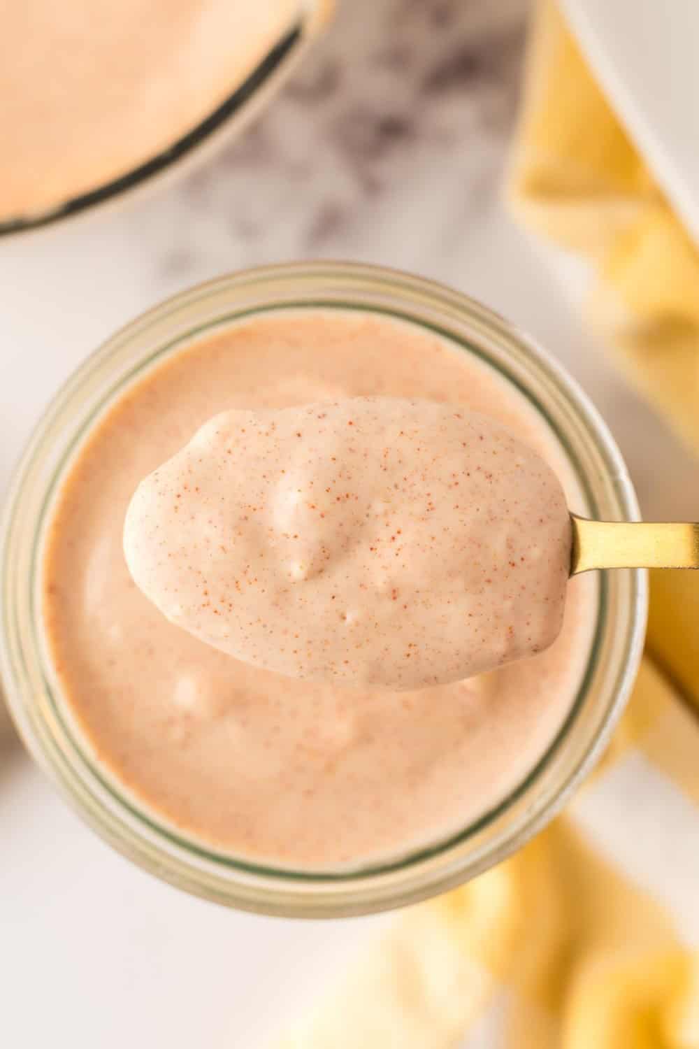 small glass jar of Alabama white sauce being spooned out with a golden spoon.