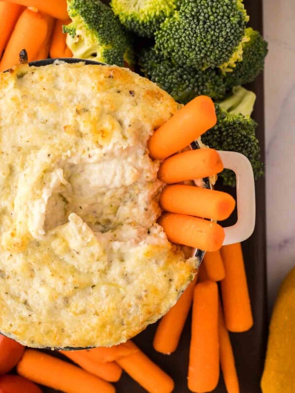 top view of carrots in a small bowl of artichoke dip recipe surrounded by other dip vegetables