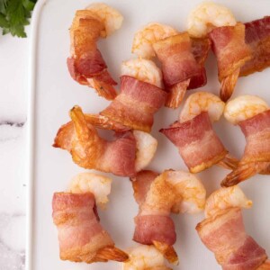 bacon wrapped shrimp recipe with lemons on a white cutting board paddle.