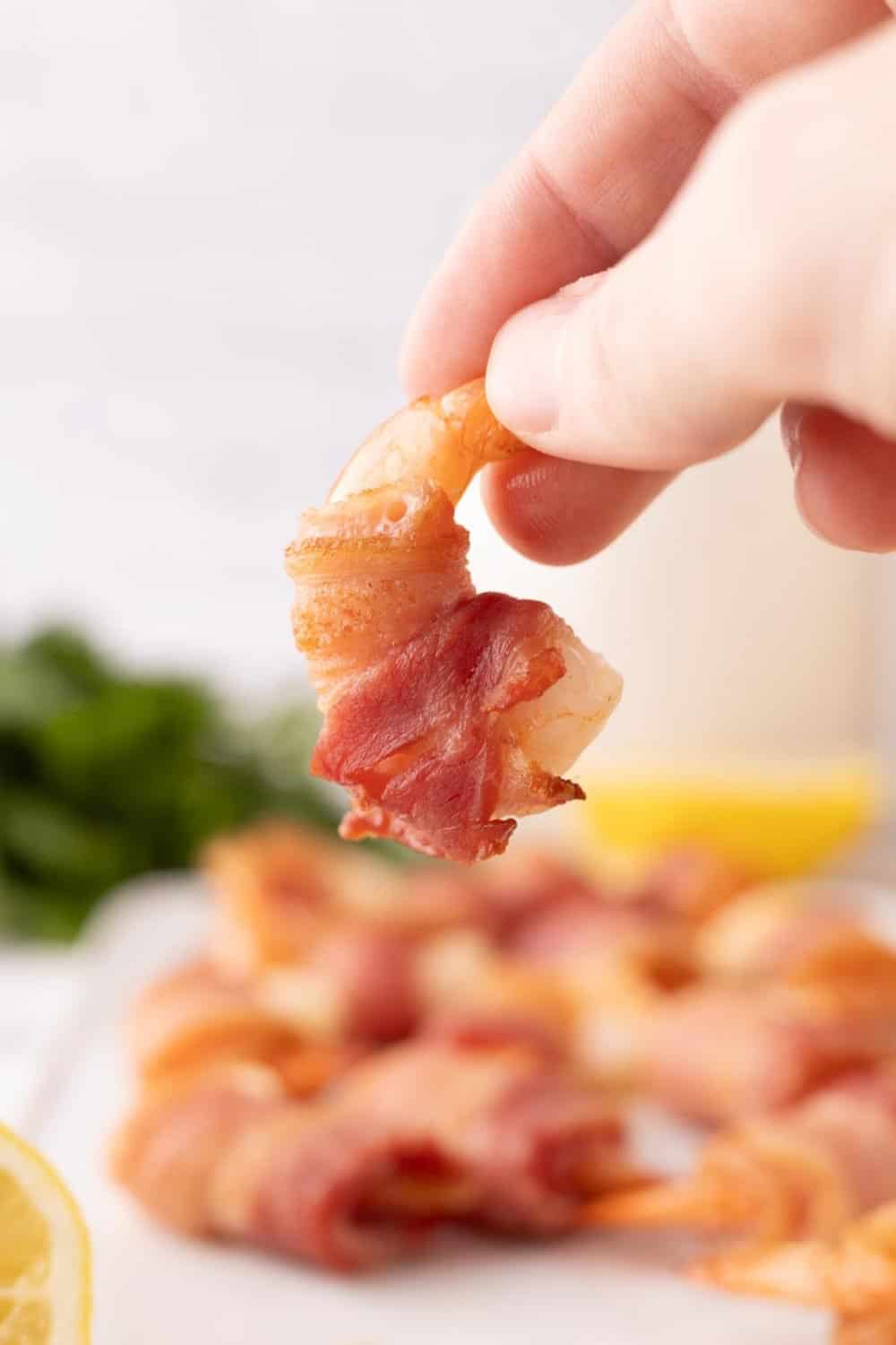 bacon wrapped shrimp recipe with lemons on a white cutting board paddle.