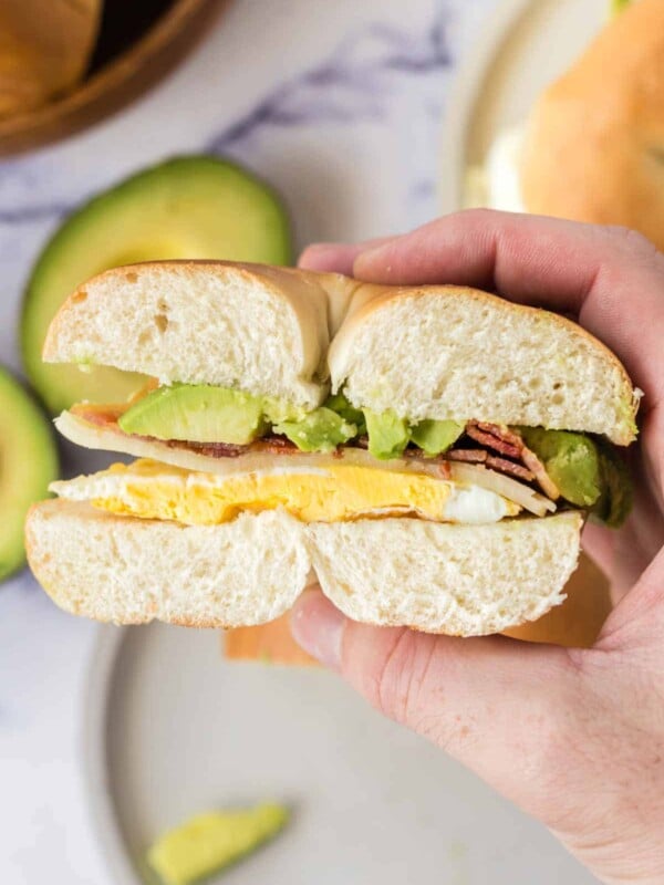 POV hand holding a side view of a half bagel sandwich