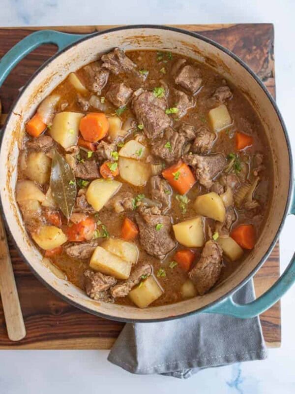 blue dutch oven with beef stew in it, looking from the top down, sitting on a cutting board garnished with chopped greens