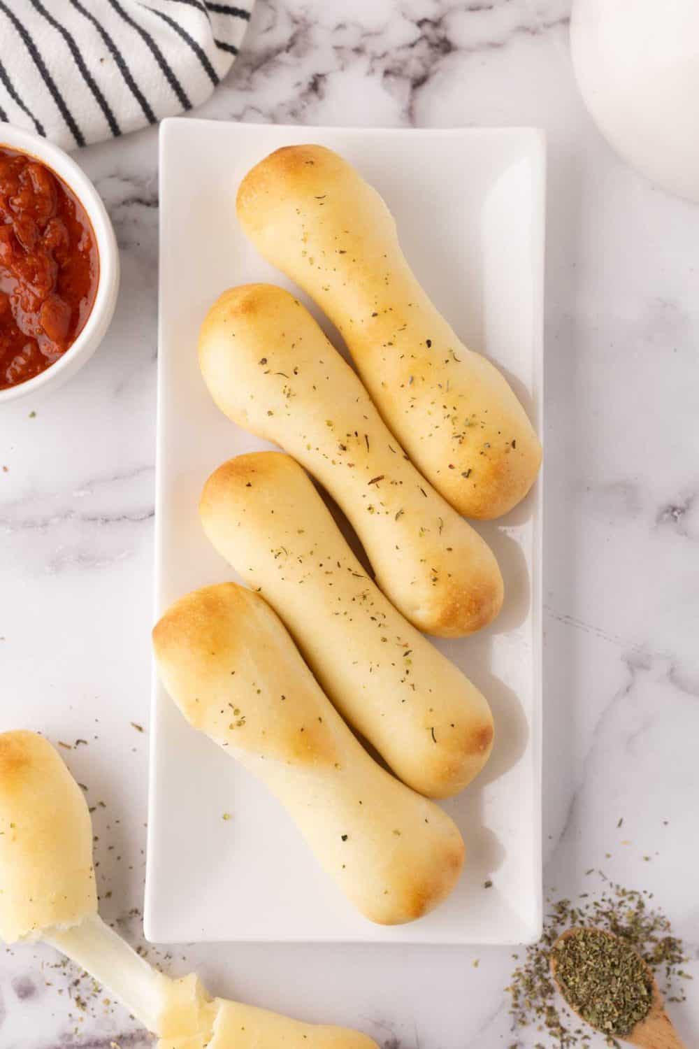 four bosco sticks on a rectangle white plate with red sauce to the side.