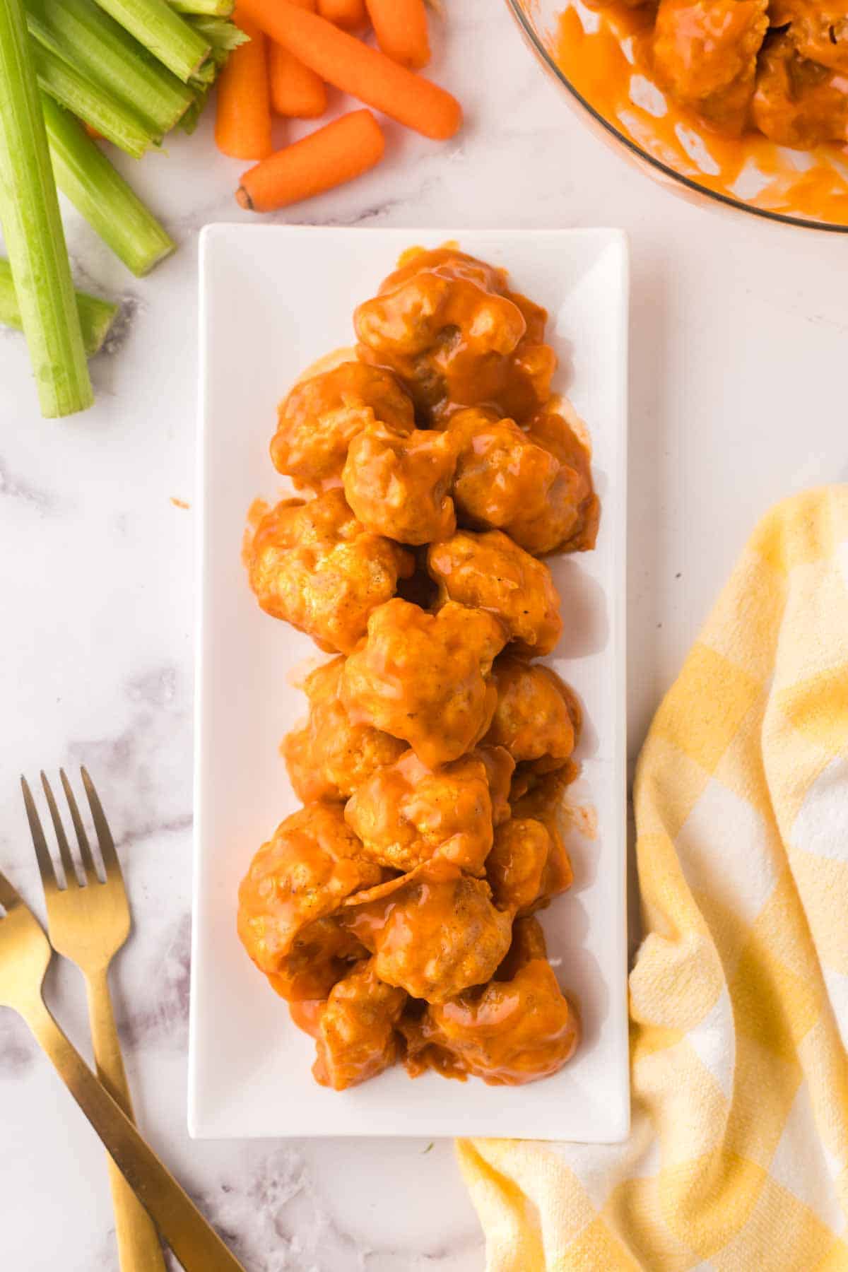 buffalo sauced cauliflower florets on a rectangle white plate with golden forks to the side.