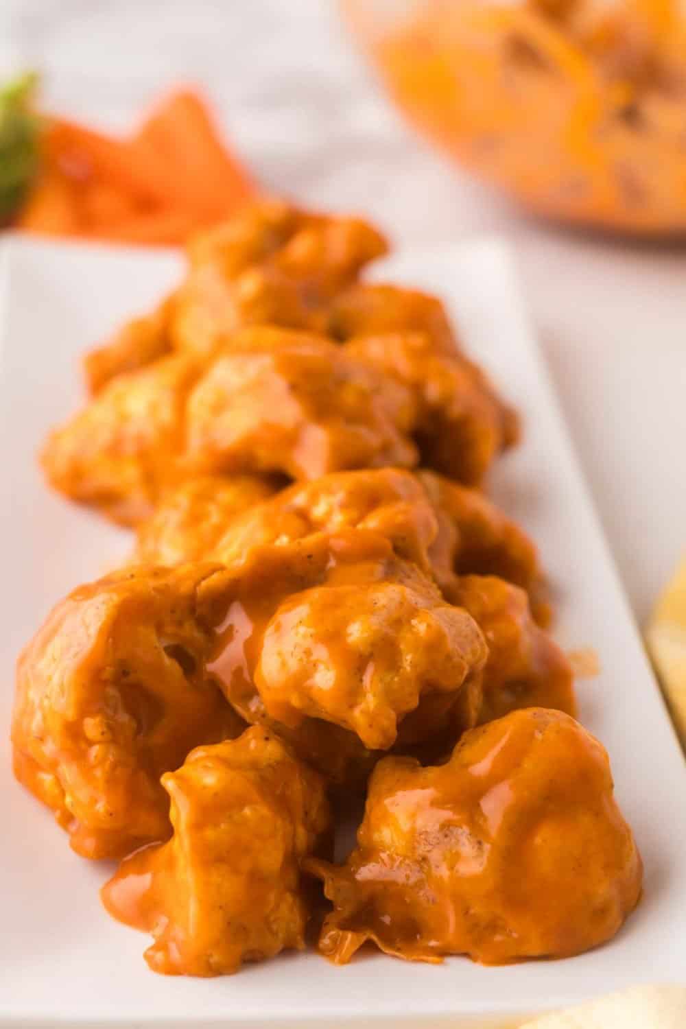 buffalo sauced cauliflower florets on a rectangle white plate with golden forks to the side.