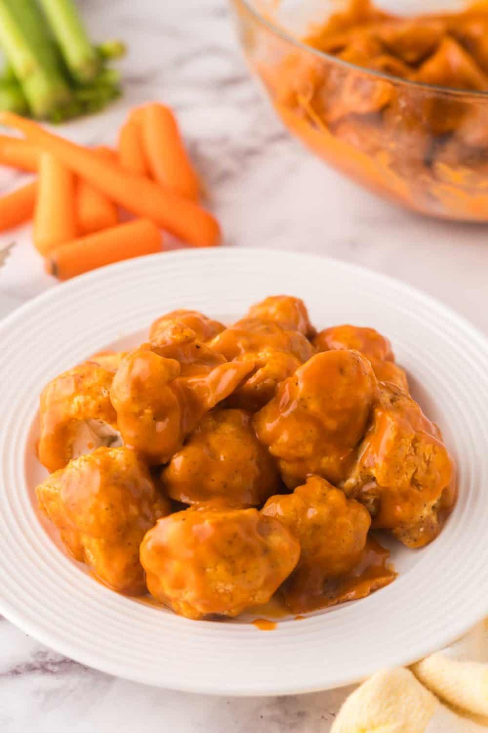 buffalo sauced cauliflower florets on a round white plate with golden forks to the side.