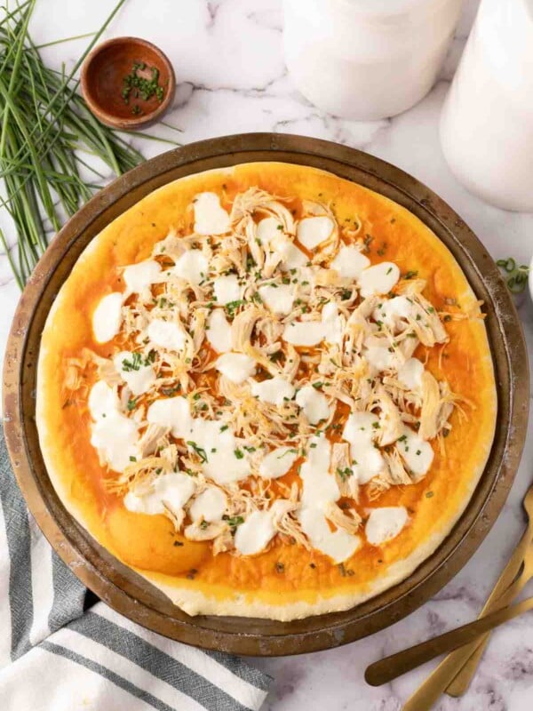 round cooking stone with raw pizza dough topped with ingredients to make buffalo pizza.