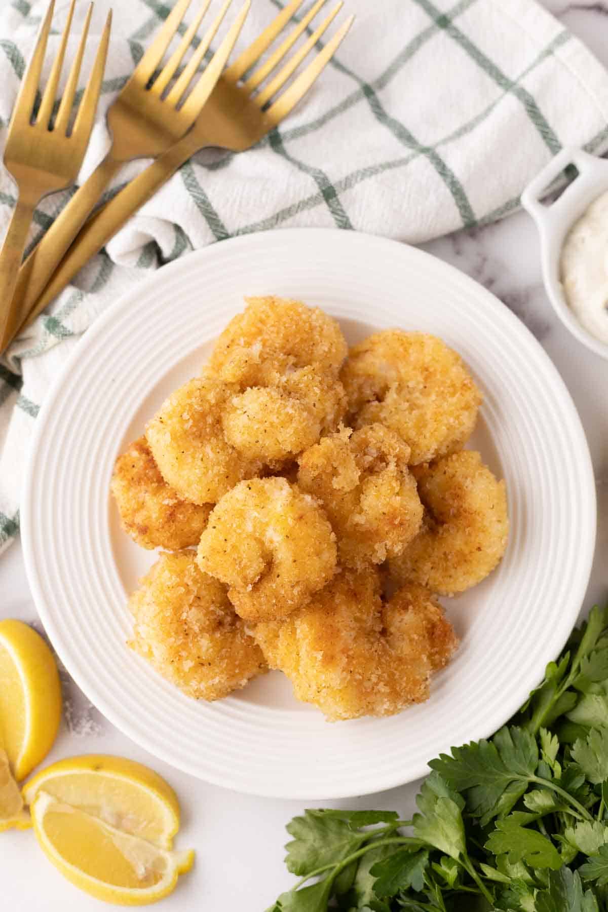 butterfly shrimp recipe on a round white plate with lemon wedges.