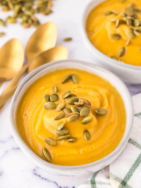 white serving bowls of roasted butternut squash soup with pumpkin seeds on top.