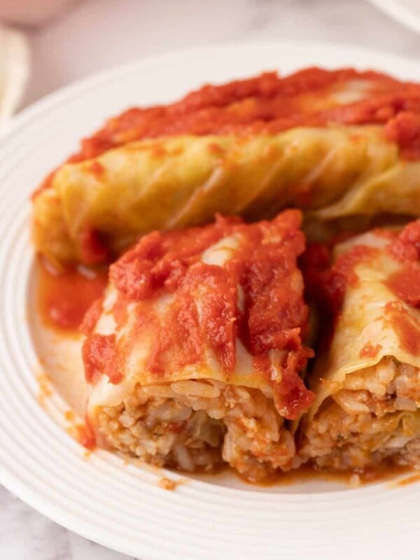 cooked cabbage rolls smothered in red sauce on a round plate sliced in half.