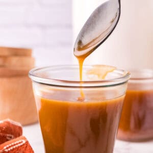 glass jar filled with homemade caramel sauce being spooned out.