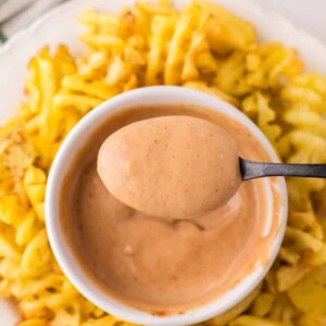 Chick-fil-A Sauce spooned out of a small bowl with waffle fries all around on a round plate.