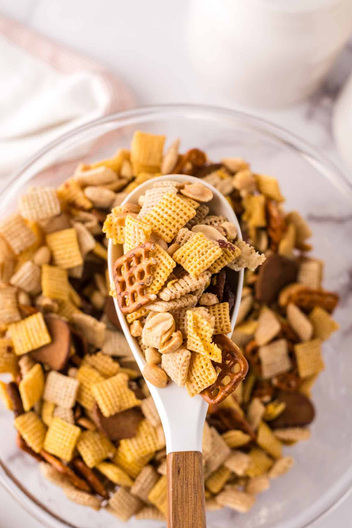 clear mixing bowl in the progress of making chex mix recipe with a wooden spoon.