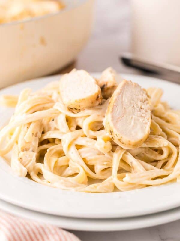 chicken fettuccine alfredo in a white serving bowl with parmesan cheese.