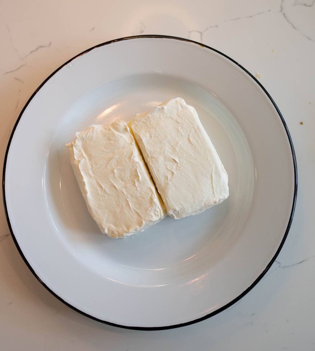 A plate with two blocks of cream cheese placed side by side on a white marble countertop.