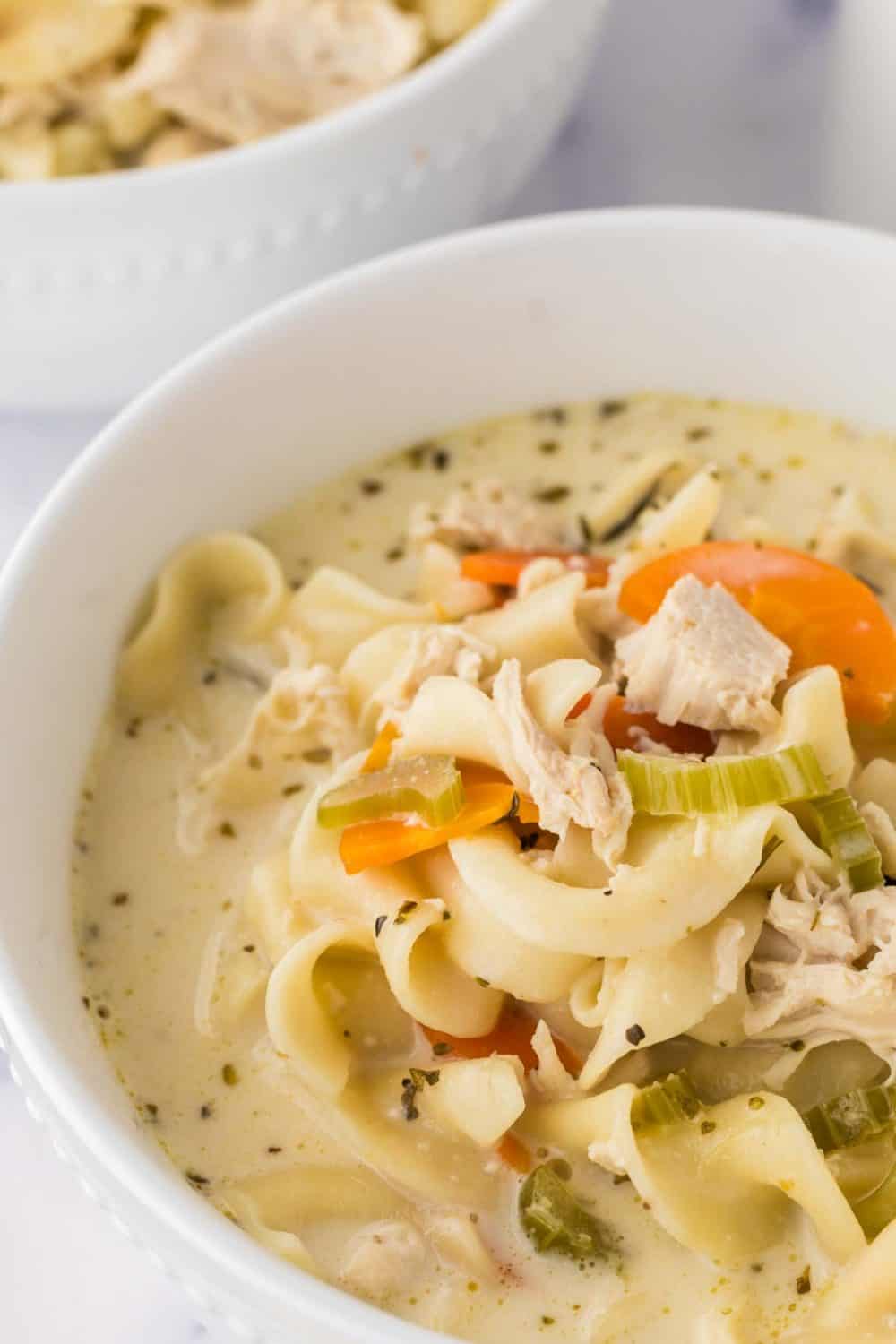 close up of a white bowl of creamy chicken noodle soup