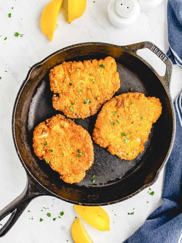 crispy fried pork chops in a cast iron skillet with lemon slices