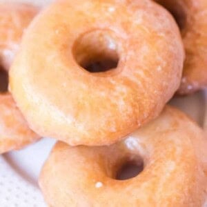 close up golden brown circle doughnut with shimmering glaze on white plate