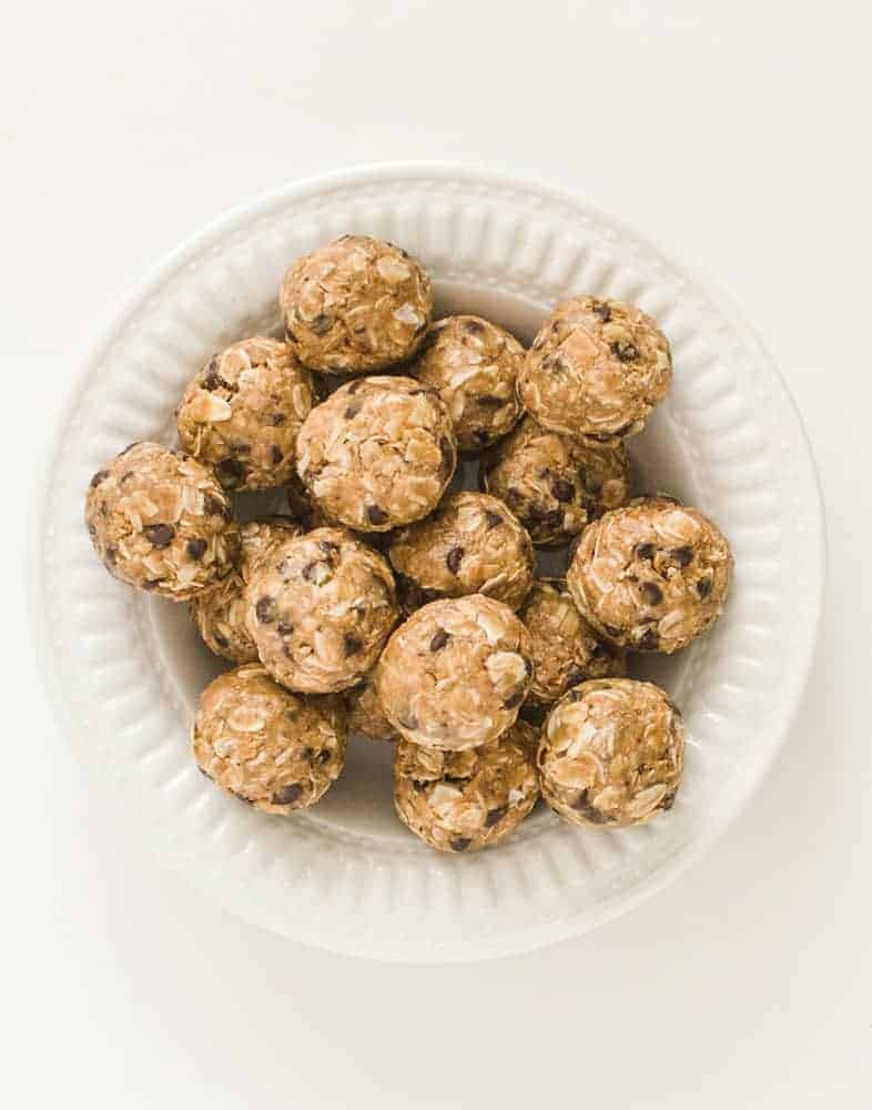 Top view of a dozen peanut butter chocolate chip oatmeal balls piled in a white bowl.