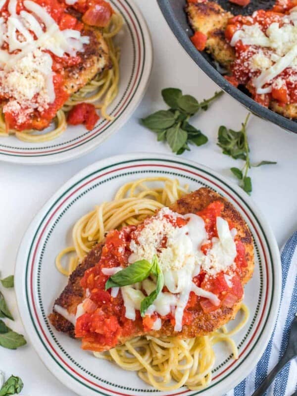 top view chicken parmesan dinner plate - spaghetti pasta and breaded chicken breast with red sauce on top on a white and Italian themed plate