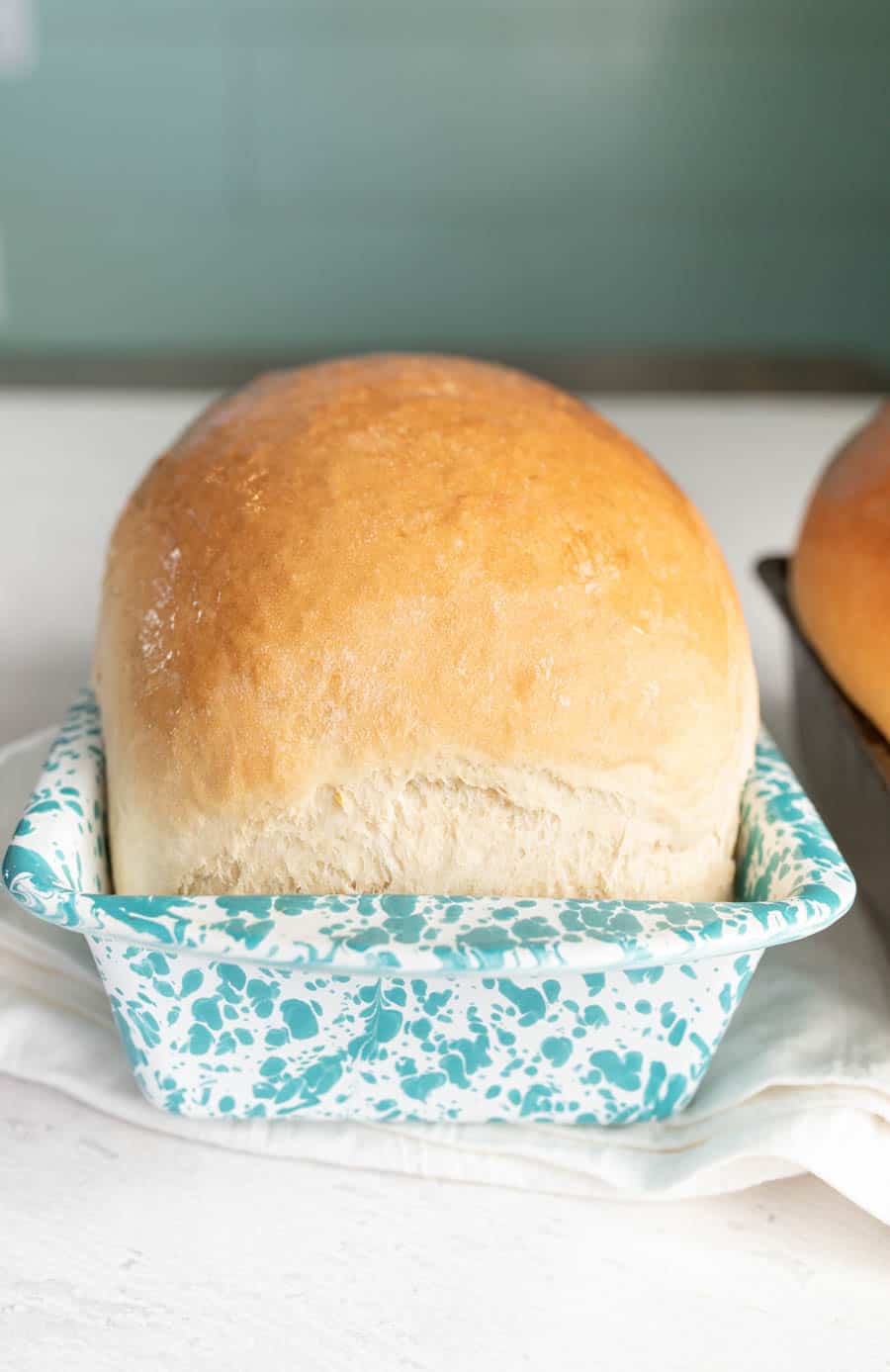 Loaf of white sandwich bread in a white and blue speckled loaf pan after baking. 