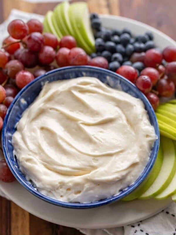 fruit dip in a bowl with grapes blueberries and green apples sliced around it