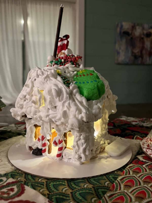 The best gingerbread recipes with a gingerbread house covered in thick white icing, decorated with candy canes, a green wreath, and Santa figurines. Its illuminated from within, sitting on a patterned cloth, creating a festive holiday atmosphere.