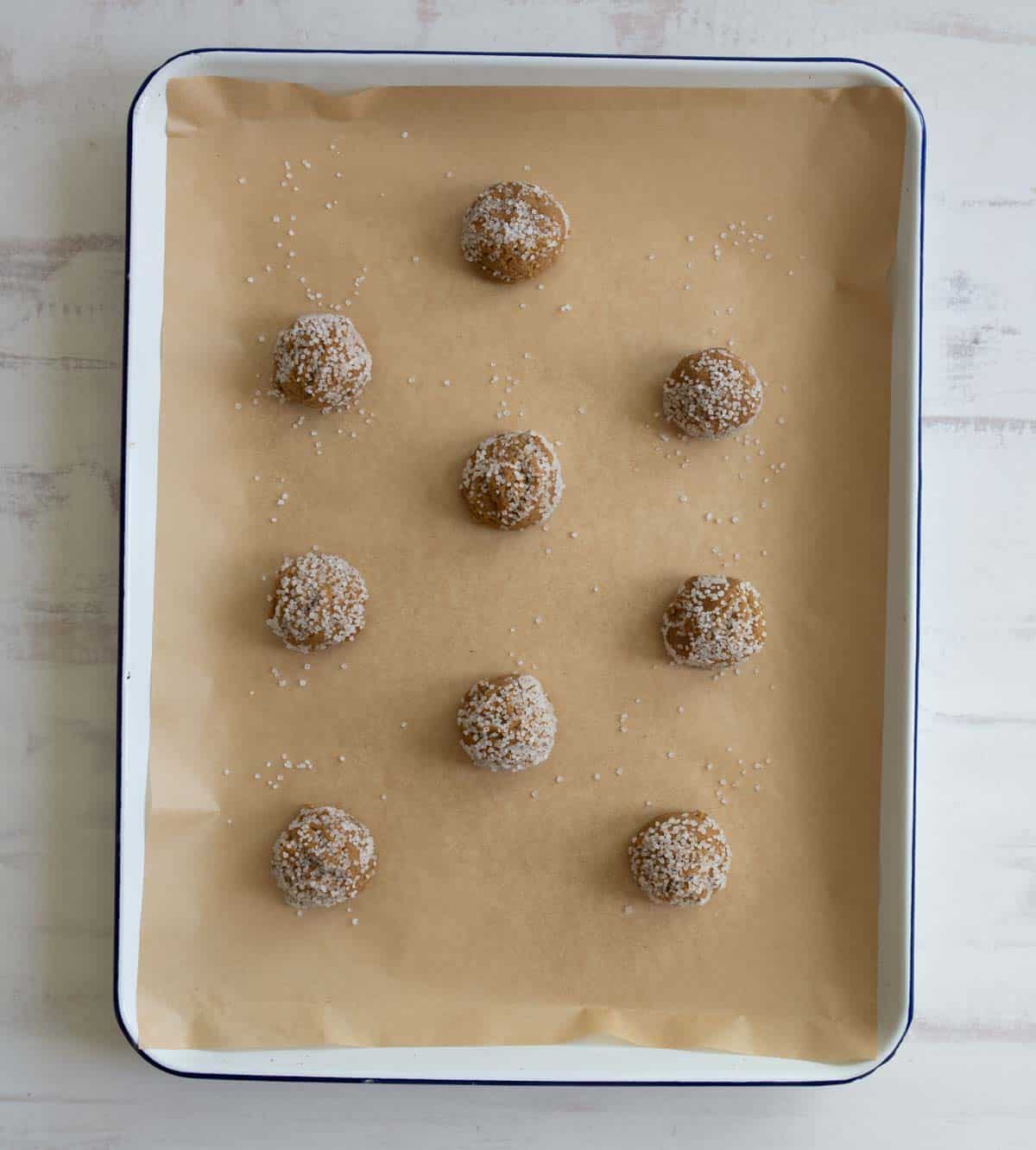 A baking sheet lined with parchment paper holds nine evenly spaced cookie dough balls, sprinkled with coarse sugar.