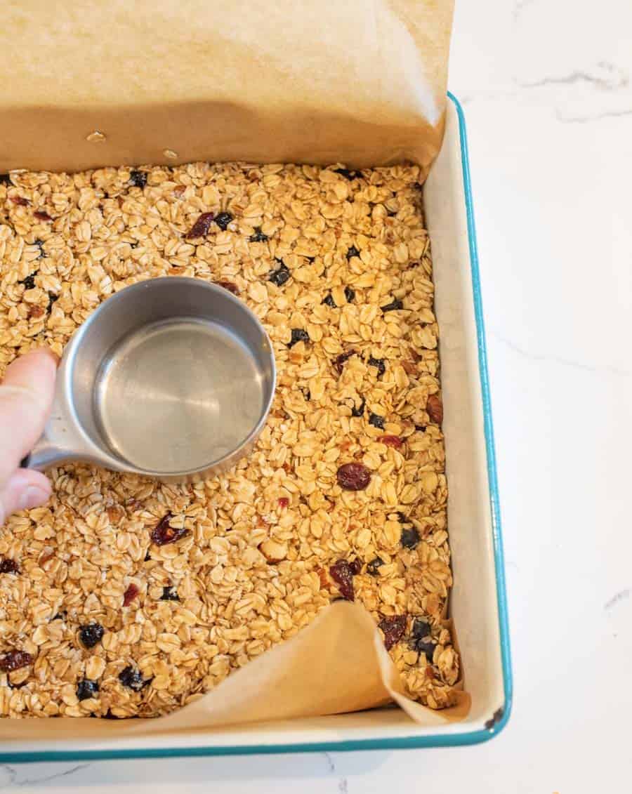 granola bar mixture being pressed into pan by measuring cup.