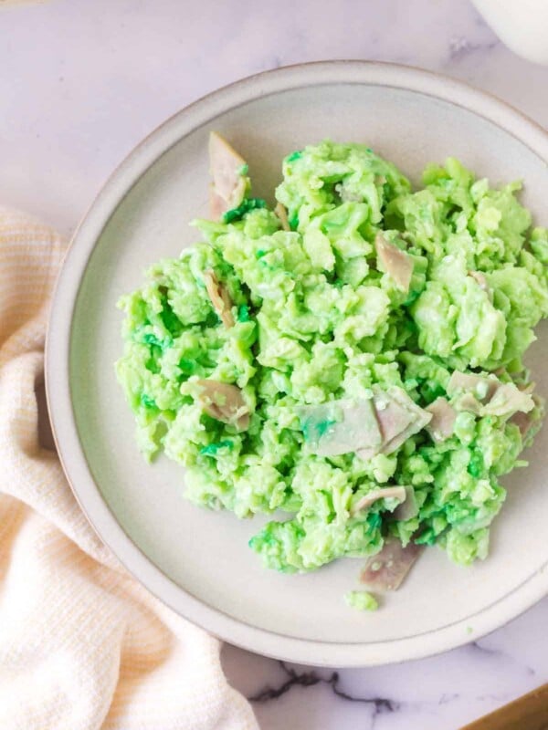 green colored scrambled eggs with pieces of ham on a white plate