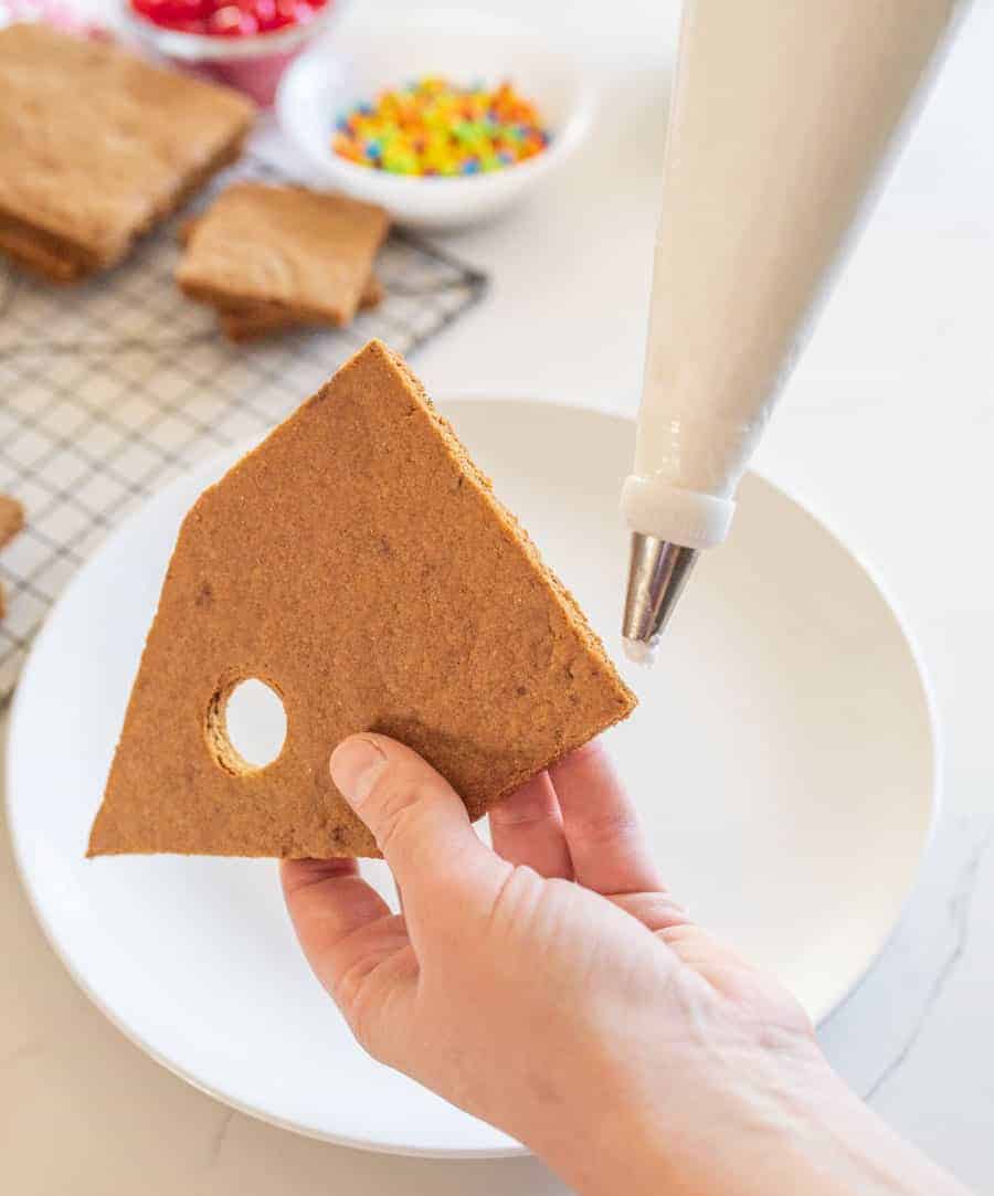 POV a hand putting icing along the bottom of a gingerbread bird house