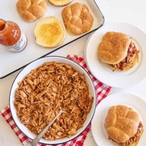 table setting of pulled pork, sandwiches on plates, toasted bun on pan.