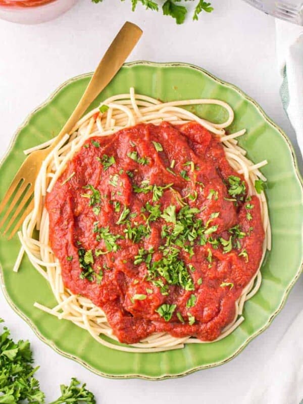 top view jade green plate with a heaping amount of sauce and fresh parsley over spaghetti pasta and a fork