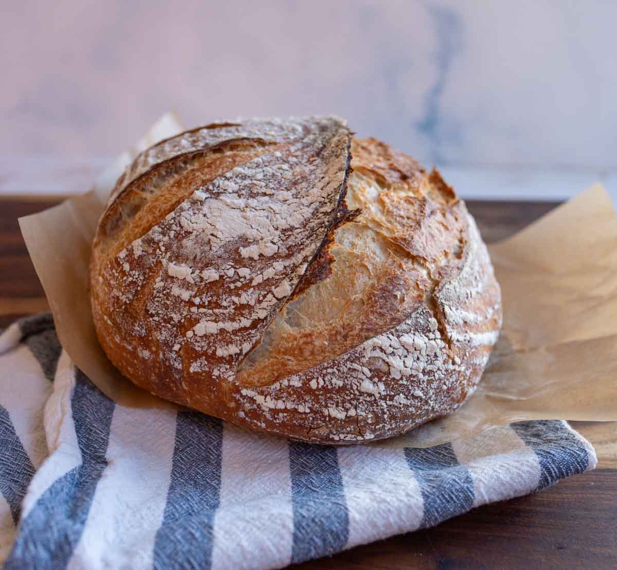 round loaf of no knead sourdough bread on blue and white towel.