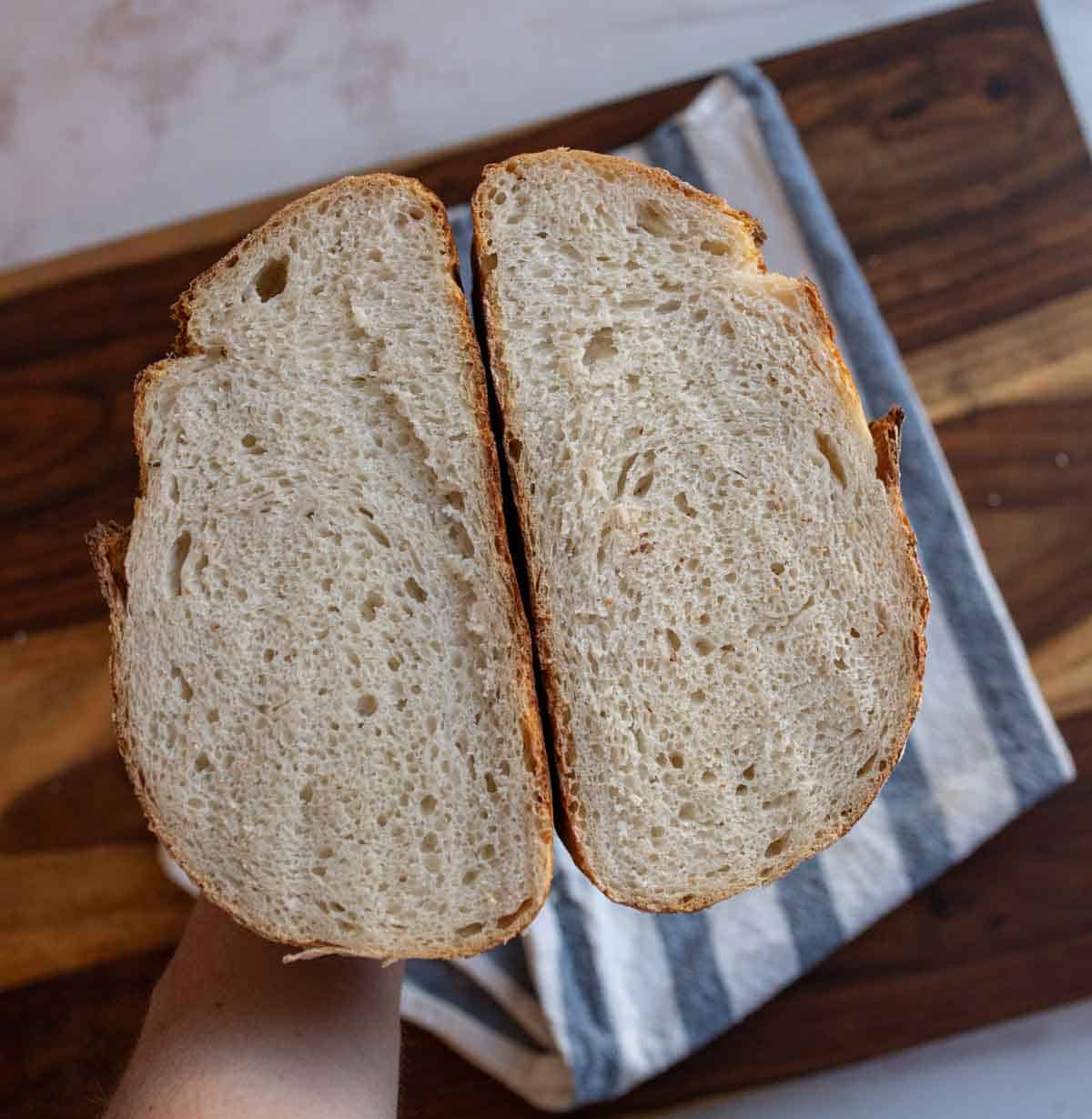 round loaf of no knead sourdough bread cut in half on a blue and white towel.