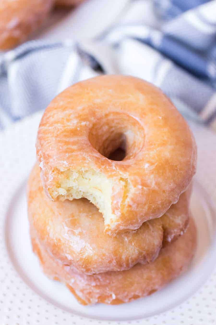 top view of a stack of old fashioned glazed doughnuts with the top one having a bite taken out.