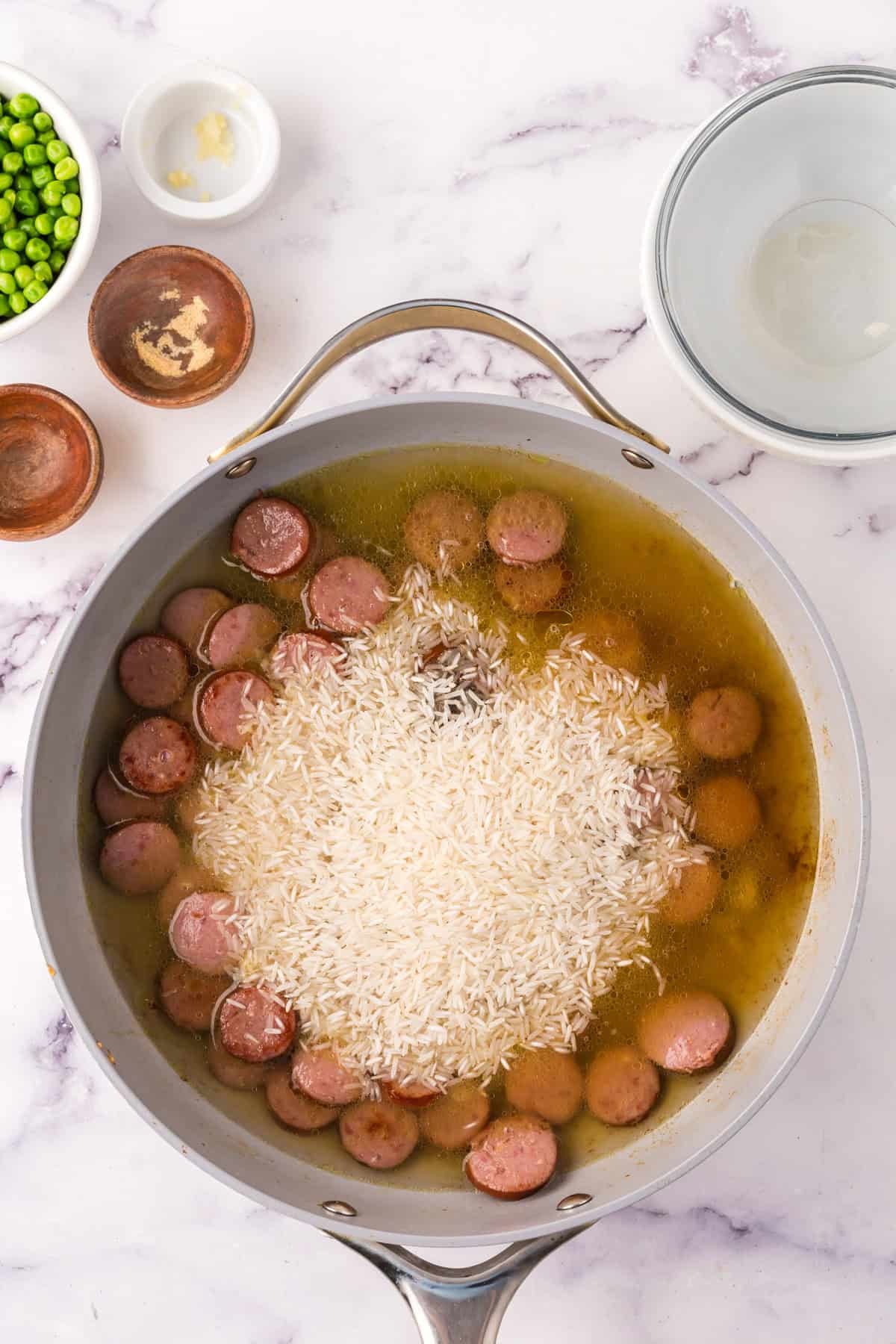 one pot sausage peas and rice in a pan in the progress of cooking.