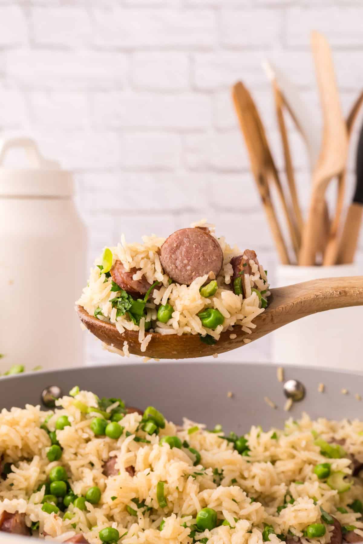 one pot sausage peas and rice in a pan in the progress of cooking on a wooden spoon.