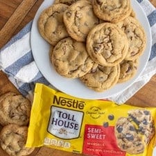 a plate stacked with chocolate chip cookies next to a bag of semi sweet chocolate morsels.