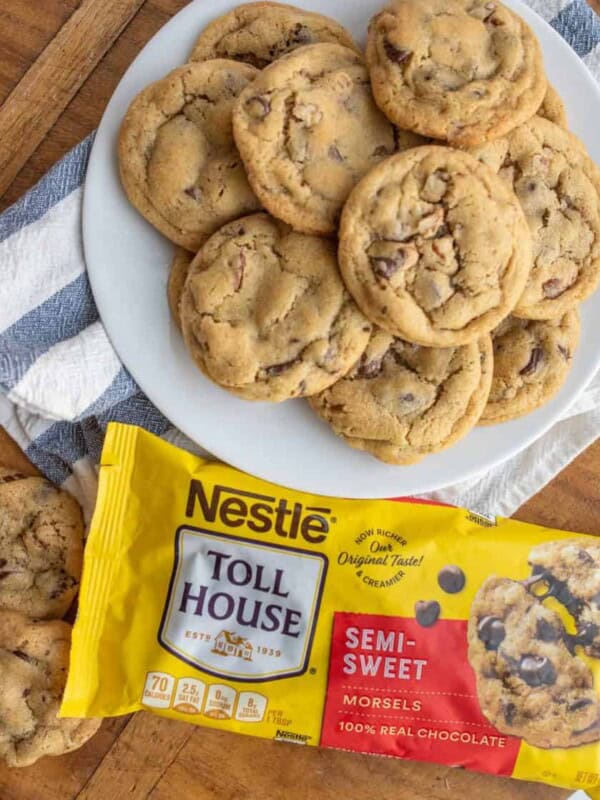 a plate stacked with chocolate chip cookies next to a bag of semi sweet chocolate morsels.