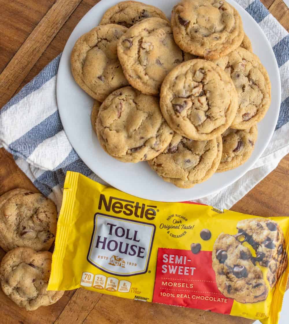 a plate stacked with chocolate chip cookies next to a bag of semi sweet chocolate morsels.