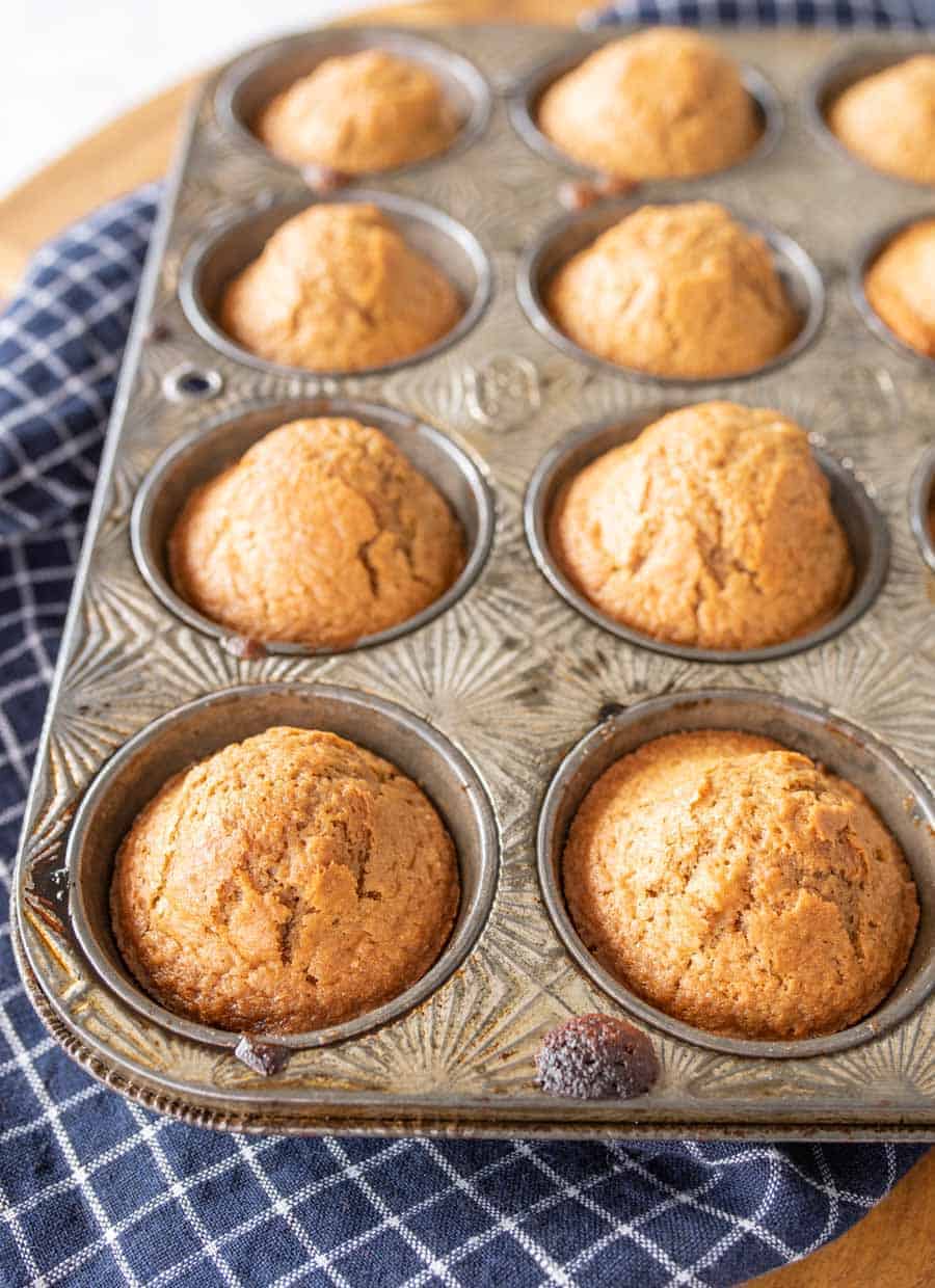 Baked sourdough muffins in a muffin pan on a blue and white towel. 