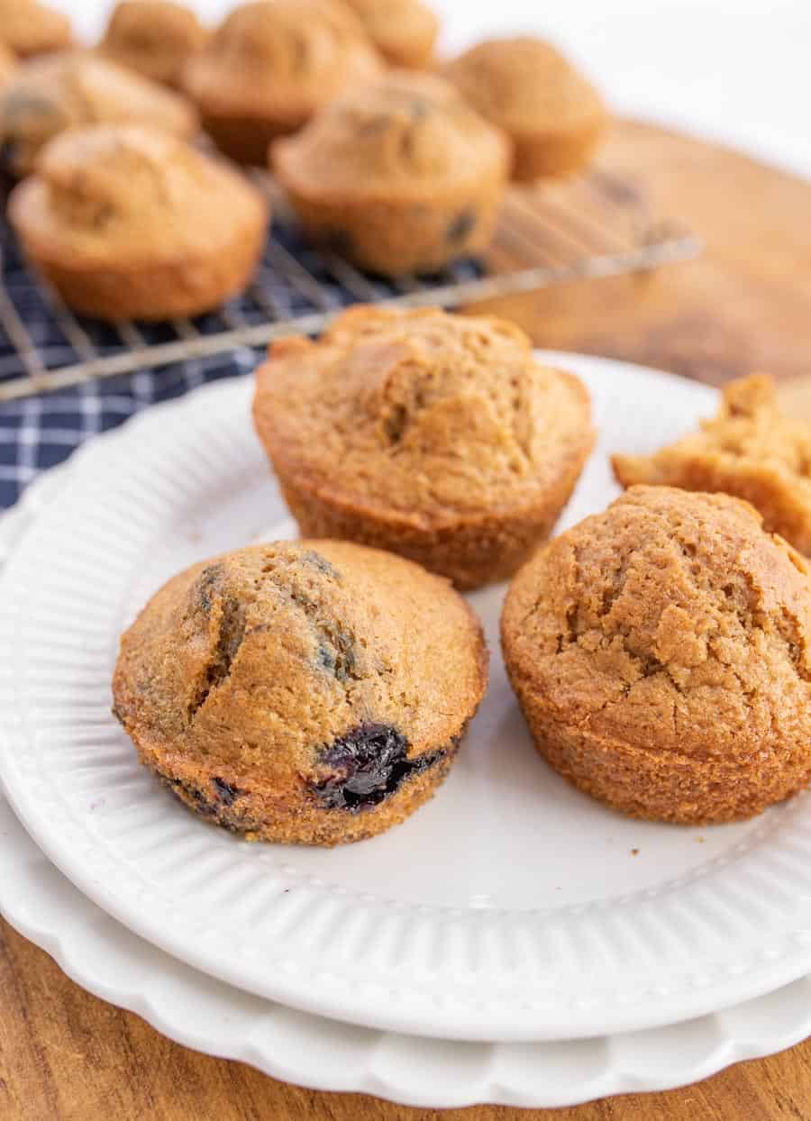 Baked sourdough muffins on a white plate where one of the muffins has blueberries in it.