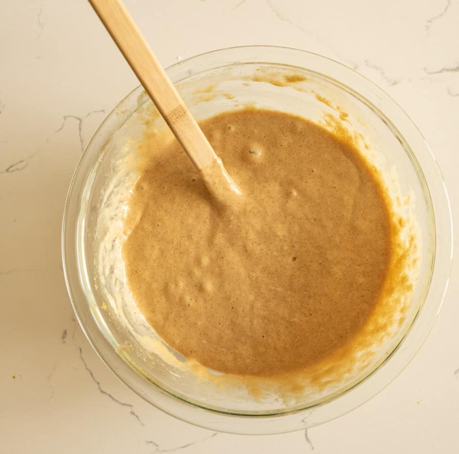 Overnight sourdough muffin batter in a clear glass bowl with a wooden spoon. 