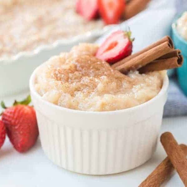 Rice pudding in white ramekin with strawberries and cinnamon sticks