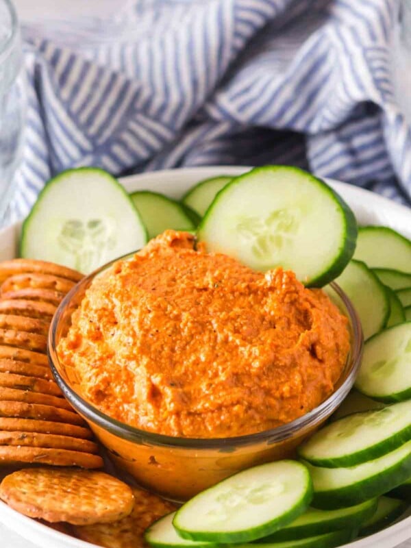 small dish with romesco sauce with crackers and chips and cucumbers around