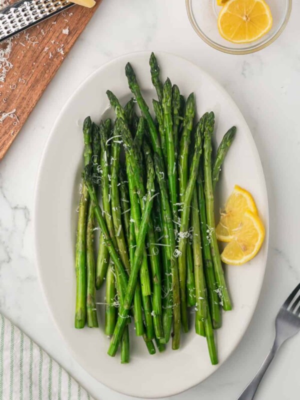 a white plate with sautéed asparagus with parmesan cheese and lemon on the side.